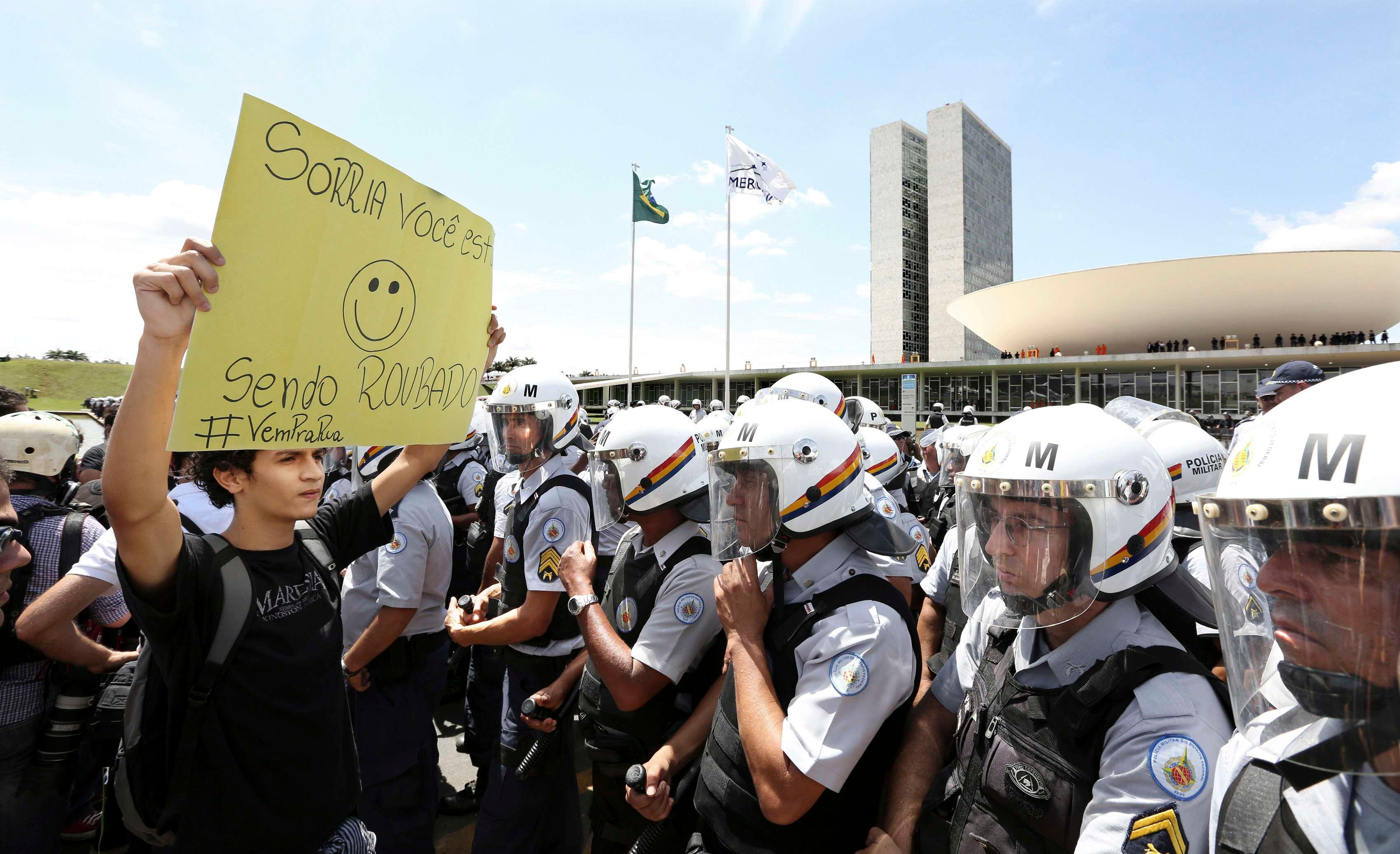 Com o Congresso Nacional ao fundo, manifestante exibe cartaz que diz "sorria... você está sendo roubado"