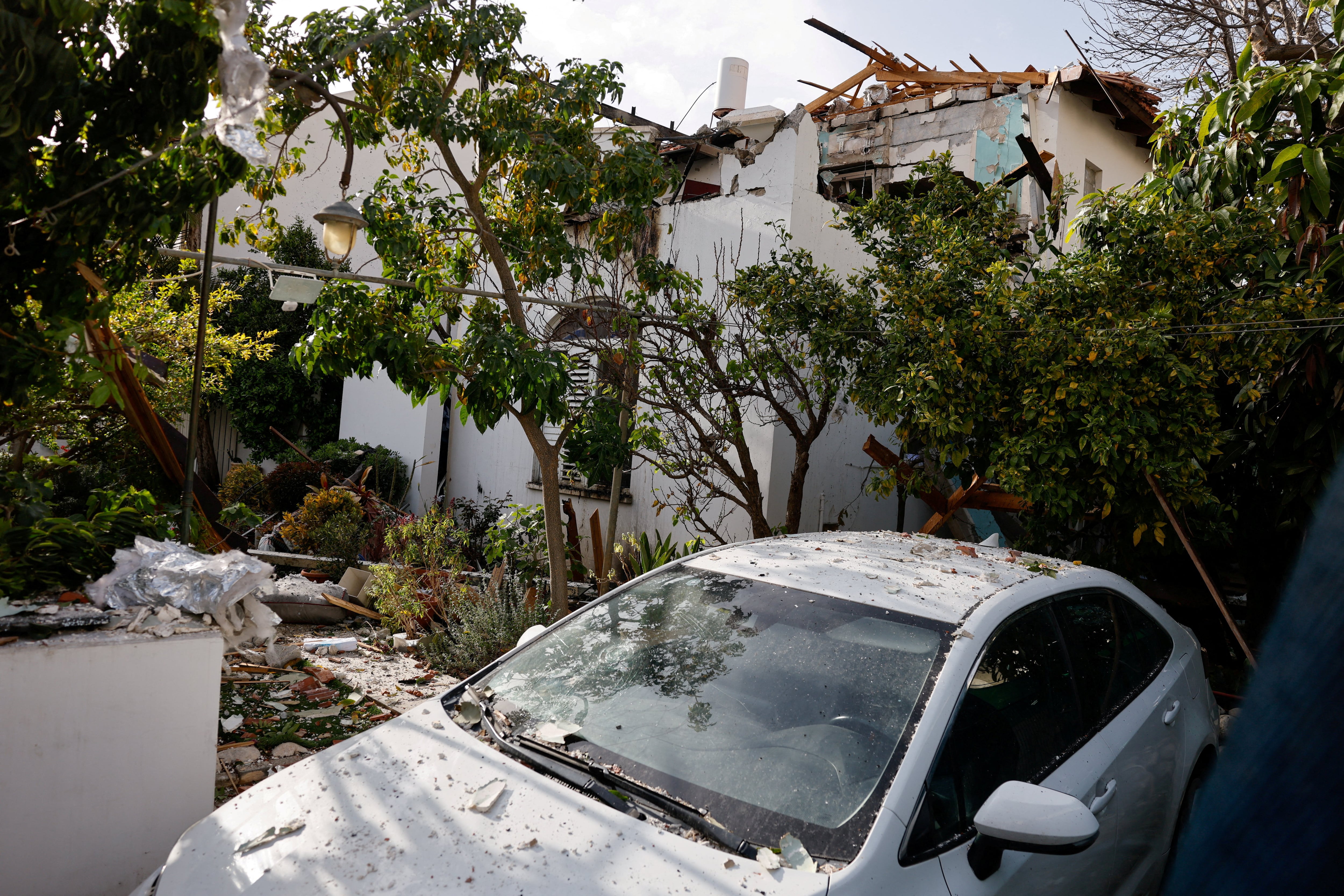 Um carro coberto de destroços ao lado de um prédio danificado em um local de impacto, após uma saraivada de mísseis lançados do Irã, em meio ao conflito entre EUA e Israel com o Irã, em Rehovot, Israel