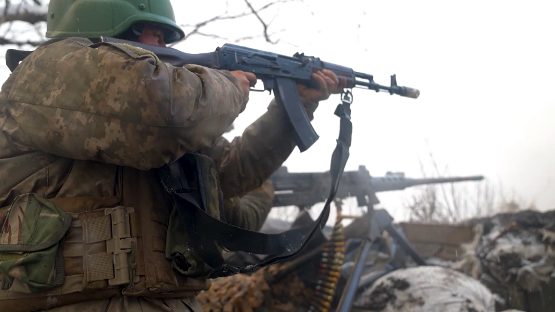 Pessoa vestindo uniforme militar e capacete, segurando e mirando um rifle em uma área externa com neblina