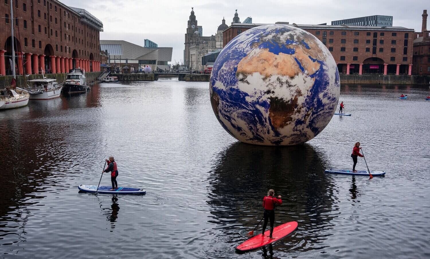O mundo gira, e o planeta continua maluco! Enquanto isso, pessoas praticam paddle board em torno da instalação de arte "Terra Flutuante", de Luke Jerram no Albert Dock, em Liverpool, no Reino Unido