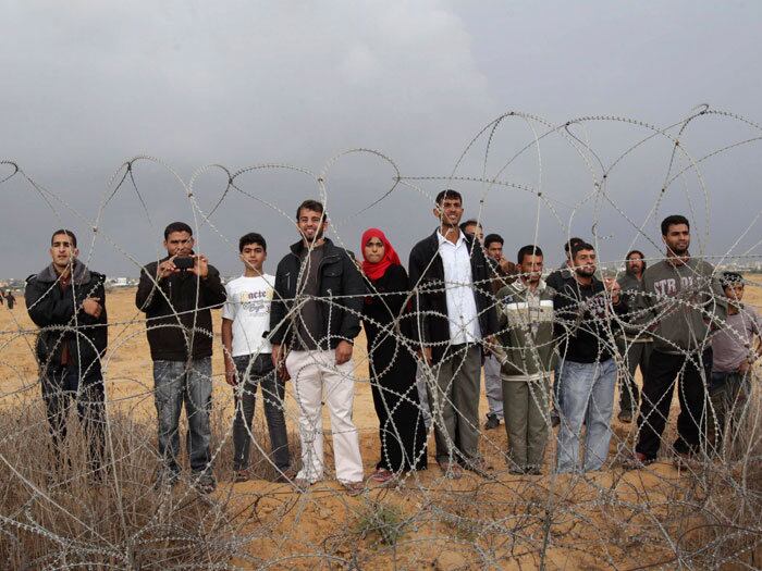 Palestinos olham para soldados israelenses que estão do outro lado da cerca que separa Israel da região sul da Faixa de Gaza
