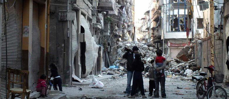 Garoto armado conversa com crianças em rua destruída de Homs, uma das cidades mais atingidas pela guerra