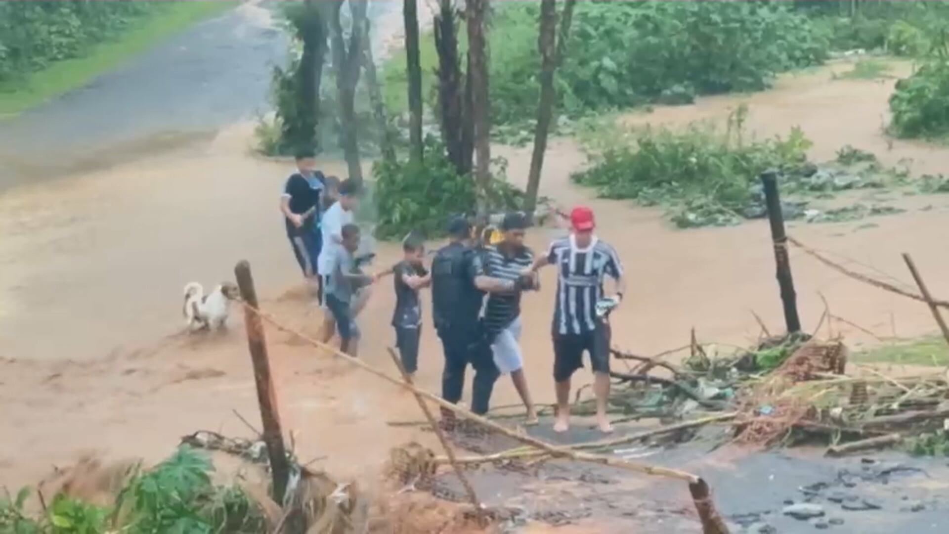 Grupo de pessoas atravessa área alagada durante uma enchente, ajudando umas às outras enquanto a água corre com força