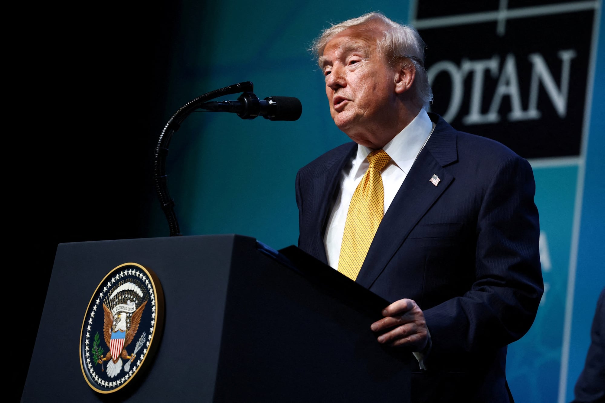 De terno e gravata amarela, Donald Trump, presidente dos EUA, em discurso em púlpito
