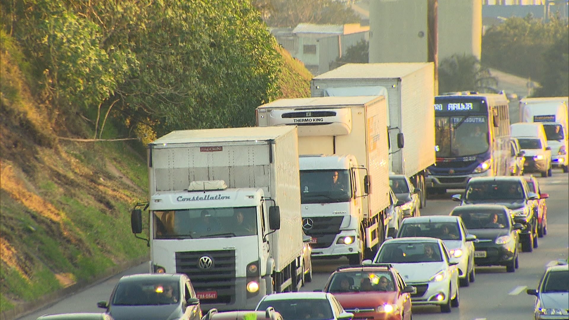Rodovia movimentada com trânsito intenso, incluindo vários caminhões e carros circulando lado a lado durante o dia