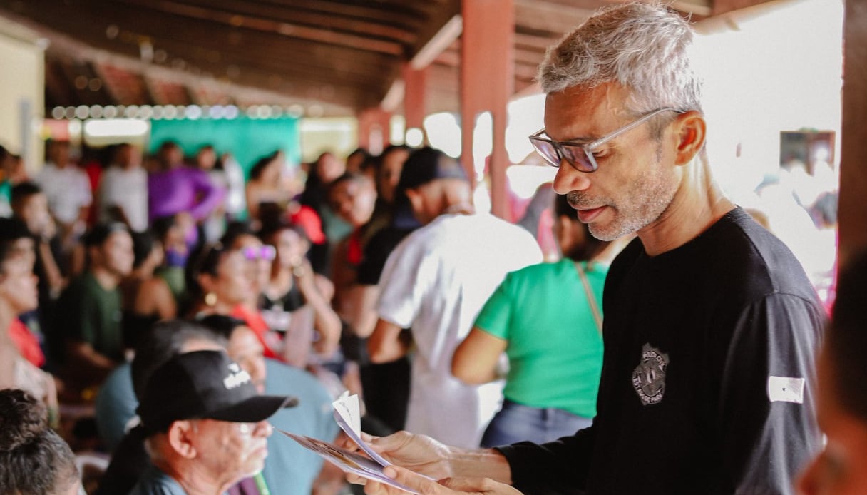 Funcionário do Incra seleciona documentos para chamar população do nordeste para regularização. Ao fundo, várias pessoas sentadas esperando