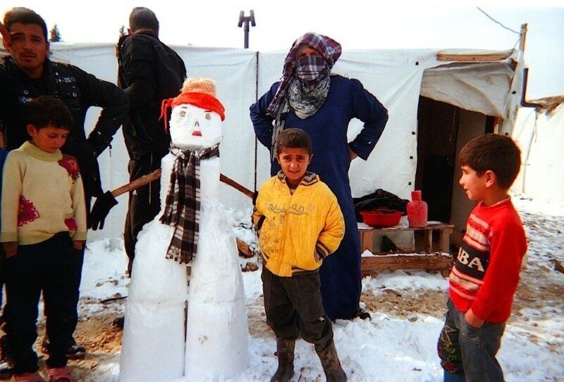 Crianças estão ao lado de um boneco de neve que fizeram fora de um abrigo improvisado. Eles foram fotografados por Akram, de 8 anos