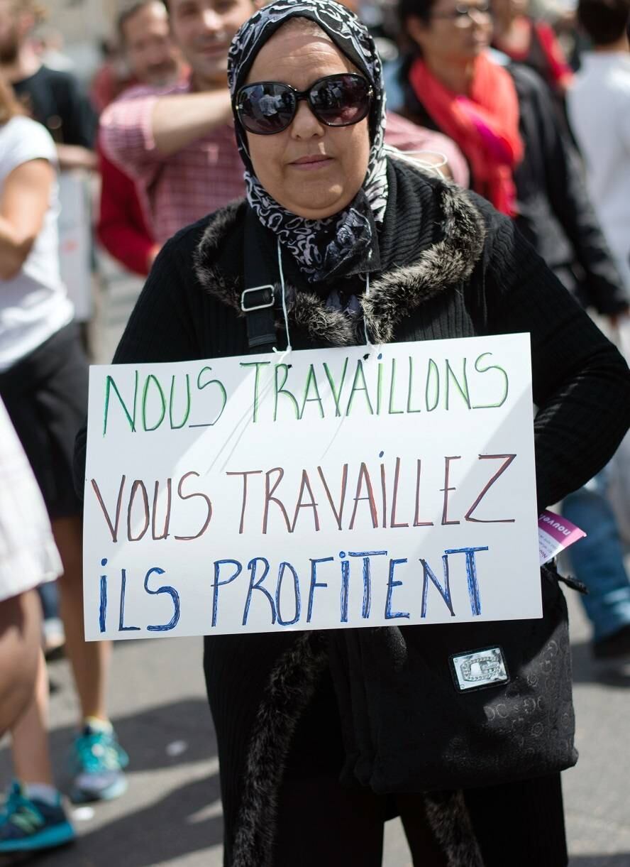 Na França, uma mulher segura um cartaz escrito "Nós trabalhamos, você trabalha, eles se beneficiam"
