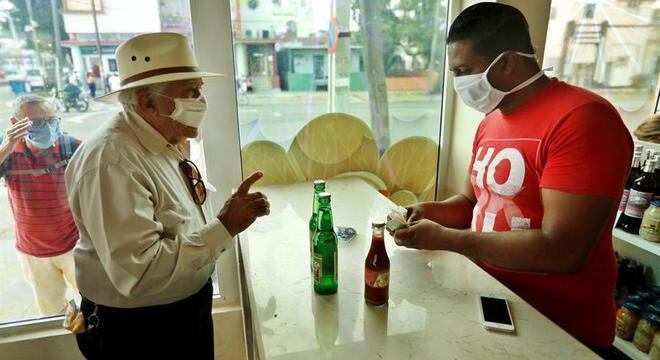 Clientes e atendente usam máscara em loja em Havana, Cuba, como prevenção ao coronavírus
