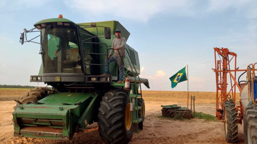 Homem parado em cima de colheitadeira no campo