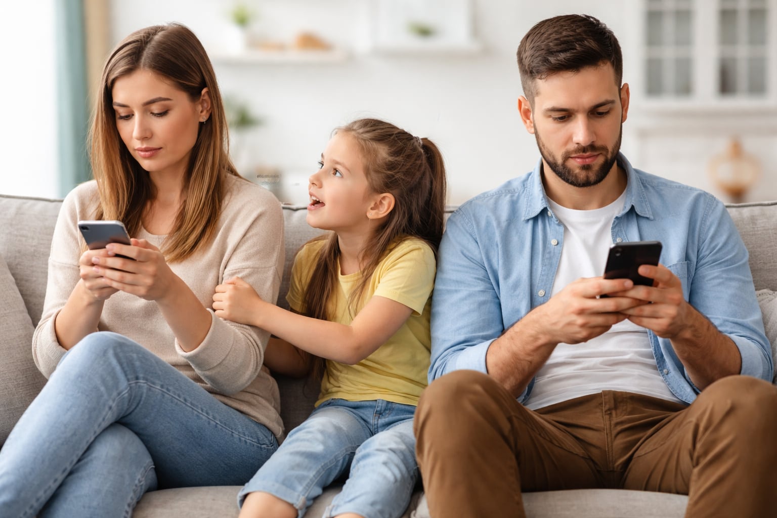 Criança tenta chamar atenção de pais que estão sentados no sofá mexendo no celular