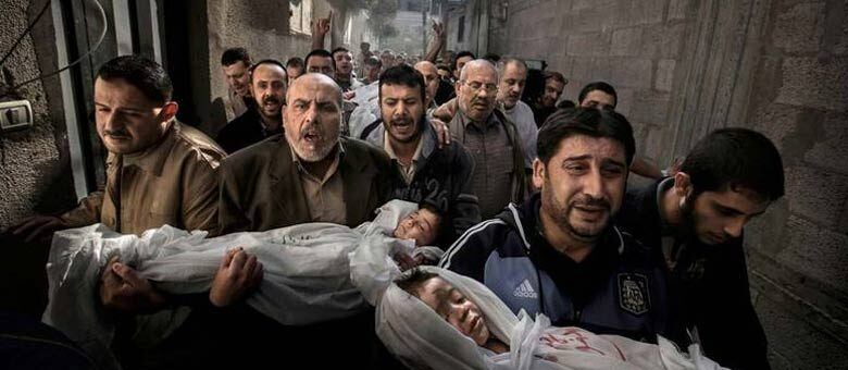 A fotografia mostra um grupo de homens carregando o corpo de duas crianças pelas ruas da cidade de Gaza