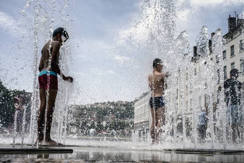 Crianças se refrescam em fonte pública em Lyon, na França, devido ao grande calor que faz na região 