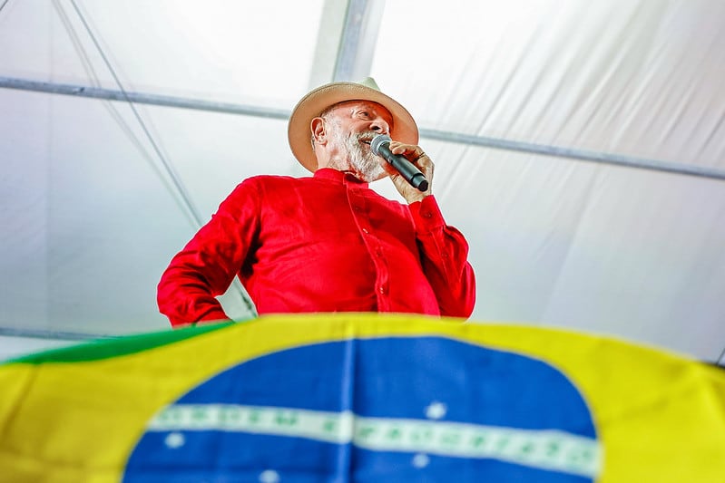 Lula de camiseta vermelho, da cor da bandeira do PT, com a bandeira do Brasil no enquadramento inferior da foto