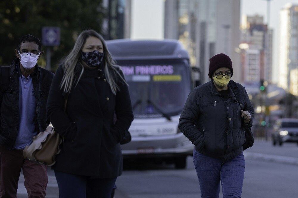 Duas mulheres usando casacos e máscaras de proteção caminham em frente a ônibus