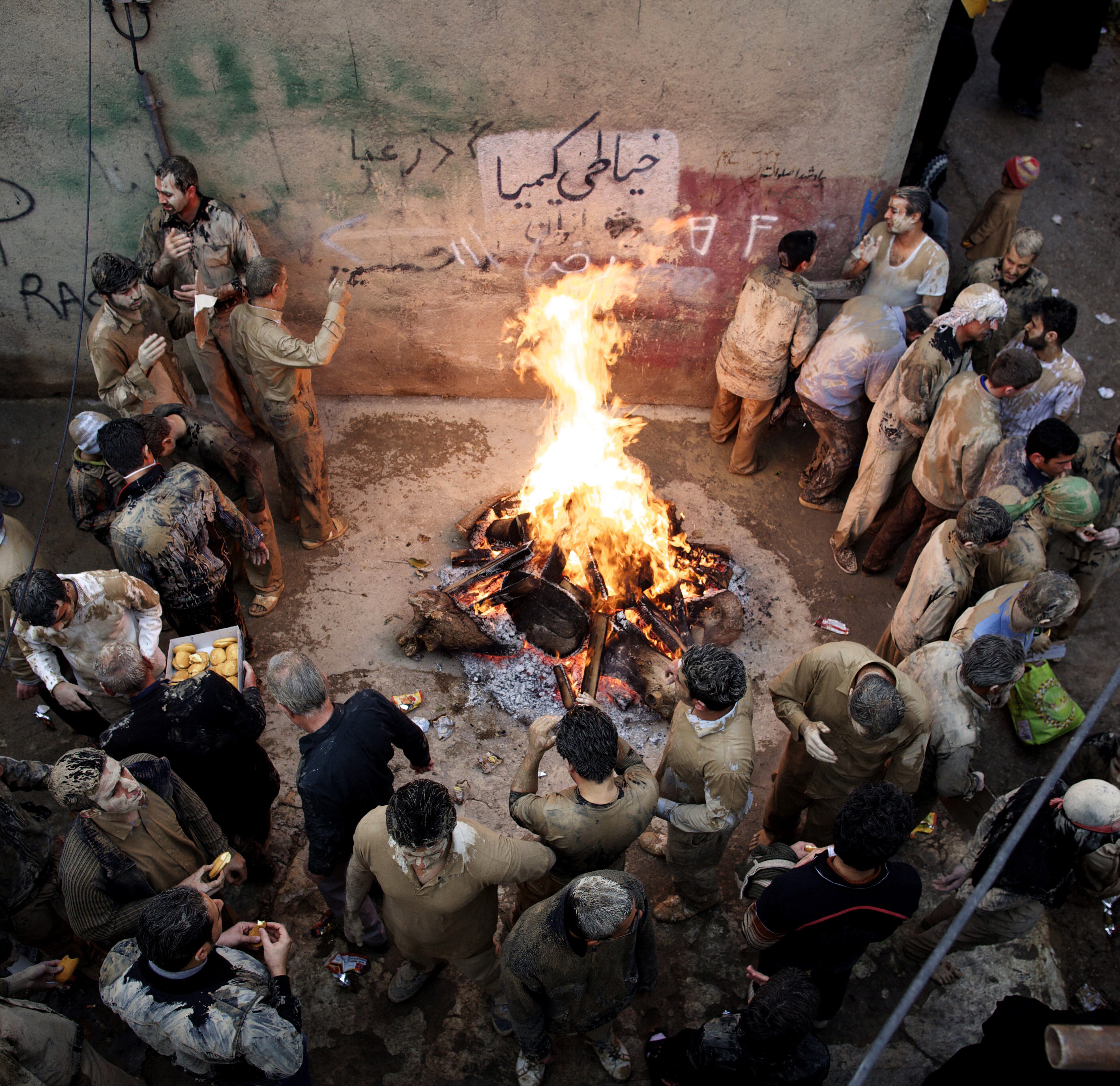 Homens cobertos de lama se reúnem ao redor de uma fogueira em Khorramabad, no Irã, antes de se autoflagelar