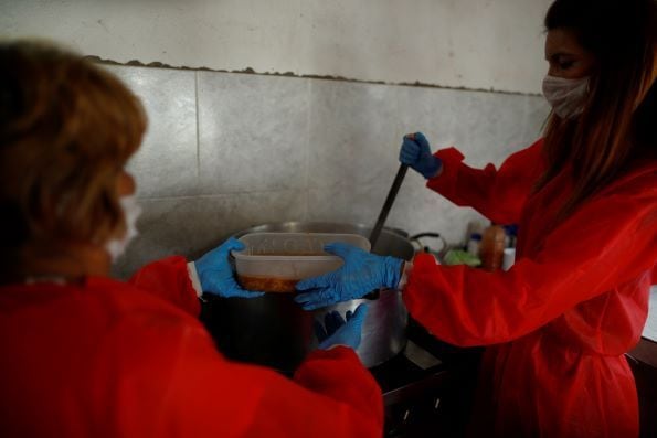 Voluntários com máscaras servem ensopado em um recipiente plástico para pessoas de baixa renda em uma cozinha de sopa durante a propagação da doença por coronavírus, em Florencio Varela, nos arredores de Buenos Aires