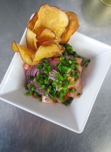 Ceviche de Salmão com Rosa de Chips de Batata-Doce
Por Rebecca Lockwood

Ingredientes:
400 g de salmão fresco sem pele e sem espinhas
2 limões
3 limões sicilianos
50 g de gengibre em conserva japonesa
1 cebola roxa
180 g de grãos de milho doce
1 pimenta dedo-de-moça
1 punhado de cebolinha
1 batata-doce
Sal a gosto
Óleo para fritura
 
Preparo:
No dia anterior, pique o salmão em cubos de 1 cm, misture o peixe com o suco de todos os limões, meia cebola roxa inteira, pimenta dedo de moça fatiada em tiras, gengibre japonês, grãos de milho doce cozidos, algumas cebolinhas inteiras sem picar e um pouco de sal. Deixe marinar por 24 horas. O sal com o doce do milho e do gengibre farão o salmão soltar um leite de tigre maravilhoso, que é o que chamamos o caldo resultante da marinada do peixe em cebola, ervas, pimenta e frutas cítricas. O leite de tigre é considerado uma iguaria, é o que confere a frescura e qualidade do prato. Para fazer a conserva japonesa de gengibre, que também serve para outros pratos como sushi, descasque 300 g e fatie no mandolim japonês bem fininho. Leve para uma panela com água fria e coloque no fogo. Quando levantar fervura, despeje a água fora. Coloque o gengibre em uma conserva de 200 ml de vinagre de arroz, 30 ml de mirim japonês, uma pitada de Aji-Sal e 5 colheres de açúcar. Deixe marinando pelo menos por 24 horas mas pode dura meses na geladeira. Se não quiser fazer, pode comprar também em lojas especializadas.
Na hora de servir, usando um mandolim japonês fatie meia cebola bem fininha e tente manter as fatias organizadas, sem soltá-las. Pique a cebolinha bem fininha.
Para preparar os chips de batata-doce, fatie a batata com casca no mandolim japonês na horizontal para fazer chips bem longos. Frite no óleo quente a 180ºC até dourarem. Escorra em papel toalha.
Prove o leite de tigre do salmão e acerte o sal. Para montar o prato, descarte a cebola inteira e a cebolinha da marinada do ceviche. Misture ao ceviche a cebolinha fresca picada e um pouco de cebola roxa fatiada. Arrume em um prato ou taça alta. Decore com cebola roxa fatiada por cima e mais ervas.
Para montar a rosa, vá encaixando os chips, um por um, em espiral na lateral do prato. Bom apetite! 
