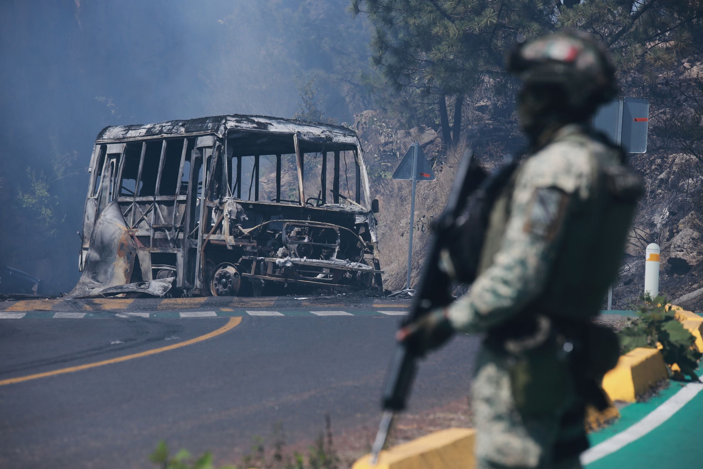 Soldado mexicano ao lado de um ônibus queimado em uma estrada