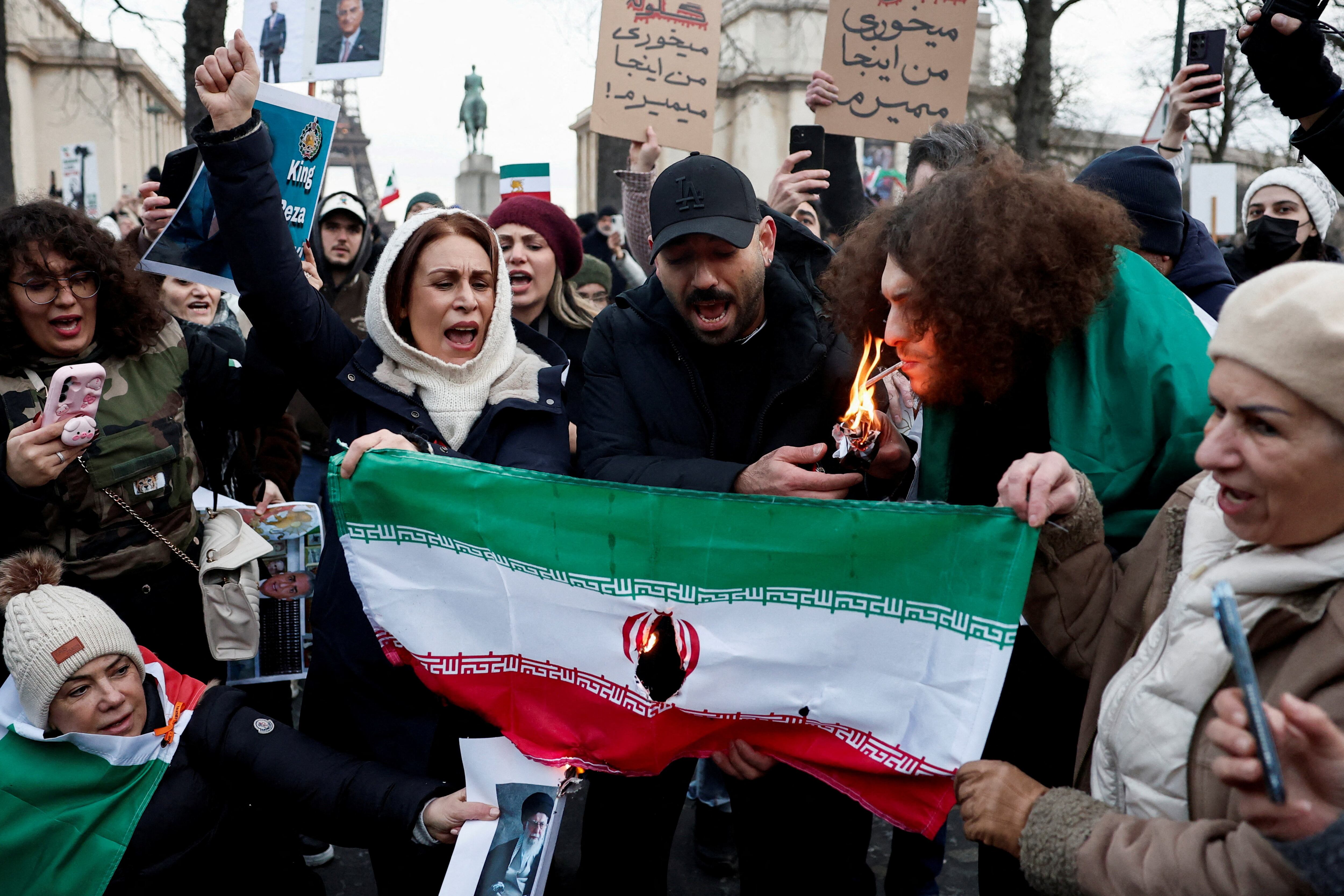 A demonstrator lights a cigarette as the Iranian National flag burns during a rally in support of Iranian people amid anti-government protests raging across Iran, in Paris, France, January 11, 2026. REUTERS/Benoit Tessier