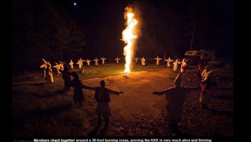 Crianças de aproximadamente 12 anos de idade, ainda não iniciadas no grupo que prega a supremacia branca, assistem de dentro de suas tendas aos adultos atearem fogo na enorme cruz de madeira