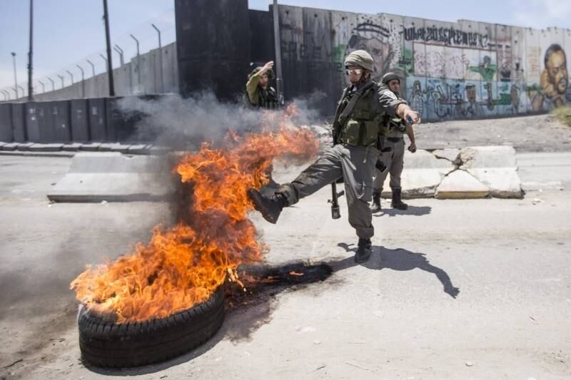 Guarda da fronteira
israelense chuta um pneu em chamas durante conflito com jovens palestinos em Qalandia