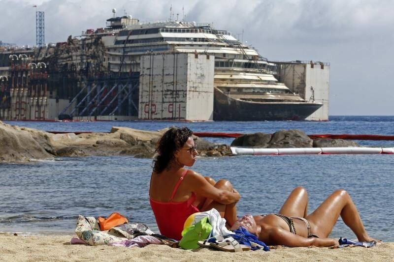 Banhistas tomam sol em
praia da ilha de Giglio com o Costa Concordia ao fundo, cruzeiro que naufragou
em 2012. A embarcação foi reflutuada e está pronta para ser retirada do local