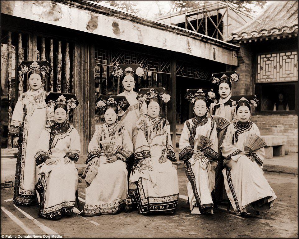 Mulheres da realeza posam para foto com trajes imperiais. A maquiagem branca sobre o rosto e os adornos sobre a cabeça ganham destaque