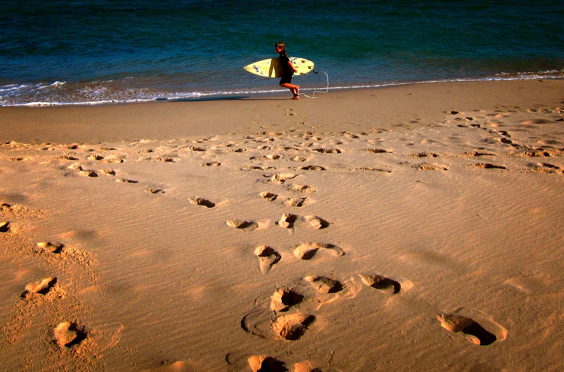 Menino de quatro anos caminha com sua prancha de surfe na praia de Mollymook, a 200 km de Sydney
