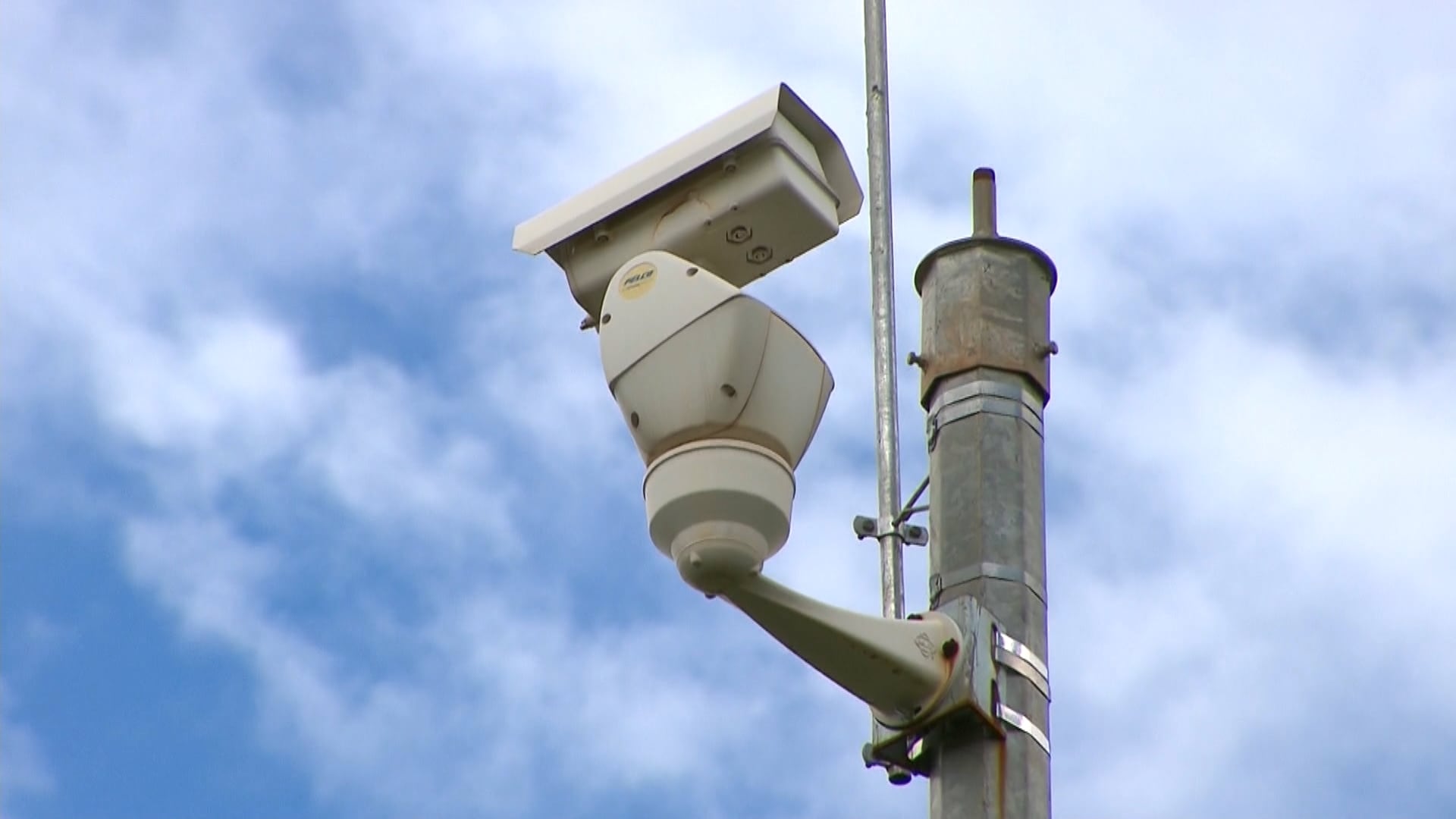 Câmera de trânsito branca fixada em um poste com o céu azul de fundo