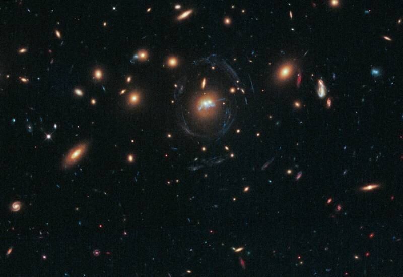 O cluster chamado de SDSS J1531 3414 tem muitas das grandes galáxias elípticas amarelas. O Telescópio Espacial Hubble mostra o centro do cluster cercado por muitos filamentos azuis finos  e curvos, que são galáxias distantes