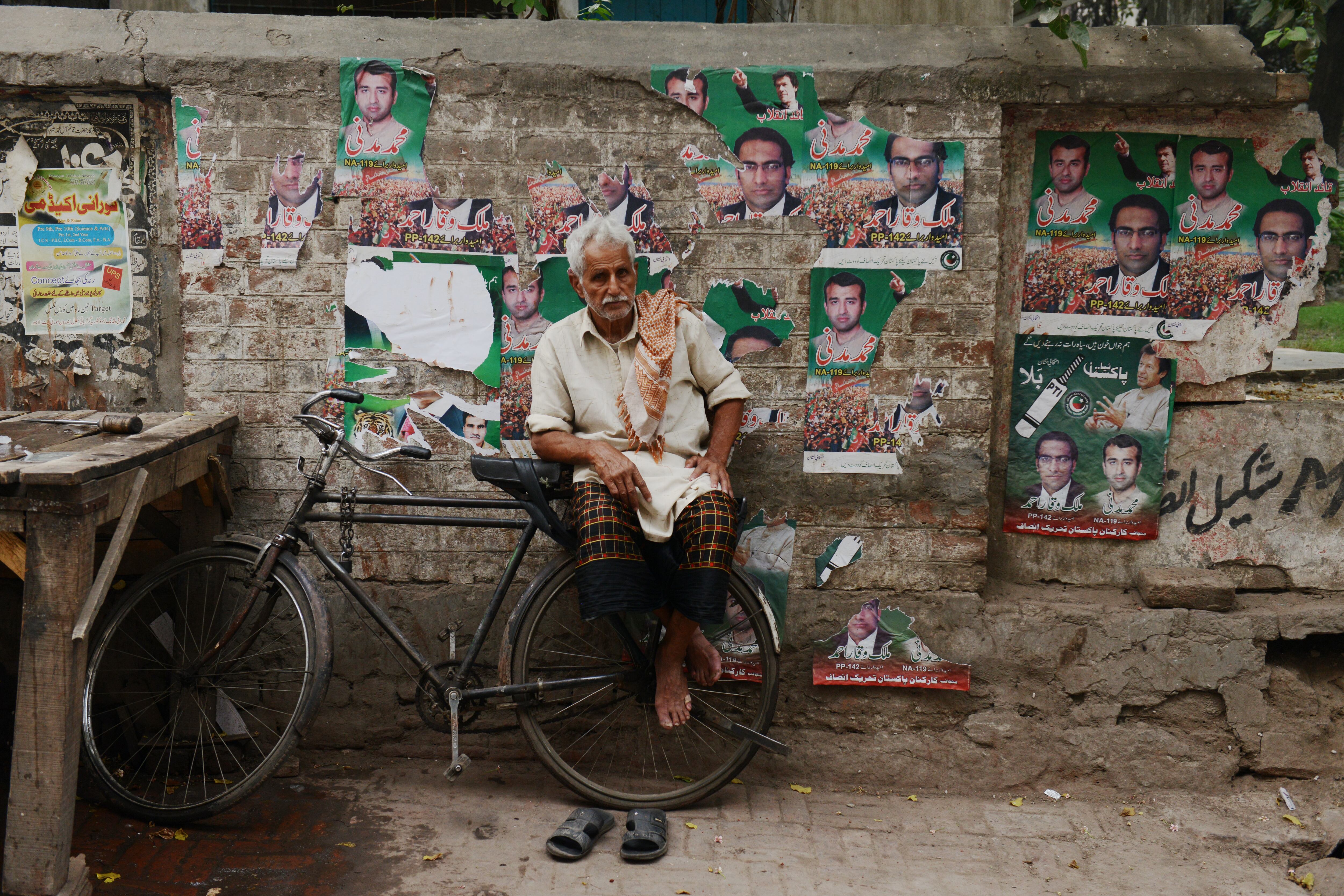 Um vendedor de gelo sentado em sua bicicleta espera por seus clientes em frente a uma parede cheia de cartazes de propaganda política em uma rua da cidade velha, em Lahore, no Paquistão