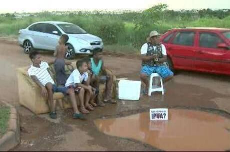 Um morador pesca no meio da rua em um buraco profundo no Arapoanga com uma faixa escrita “Cadê o dinheiro do IPVA?”