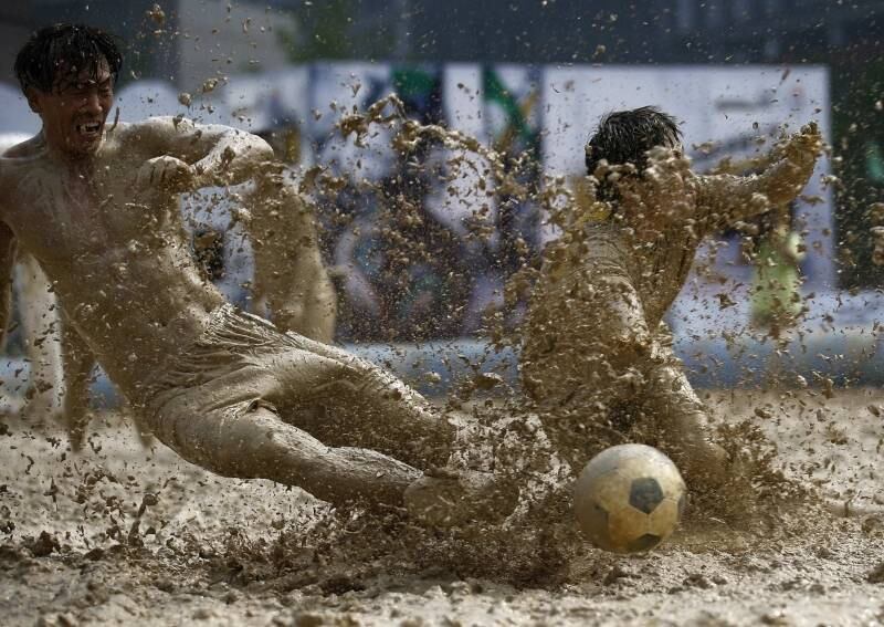Jogadores disputam por
bola durante torneio de futebol na lama em Pequim, na China