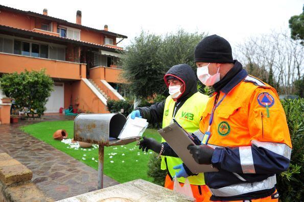Voluntários do VAB (corpo florestal) para erradicar a propagação da doença por coronavírus entregam uma máscara de porta em porta a todos os habitantes do município de Castiglione della Pescaia, Grosseto, Itália