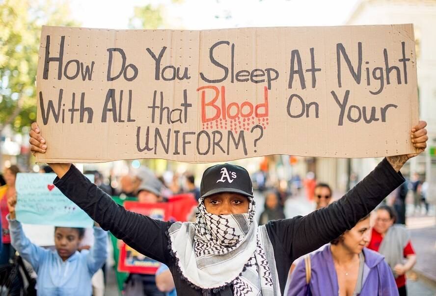 Um manifestante carrega uma placa questionando como os policiais conseguem dormir com o sangue de pessoas na farda