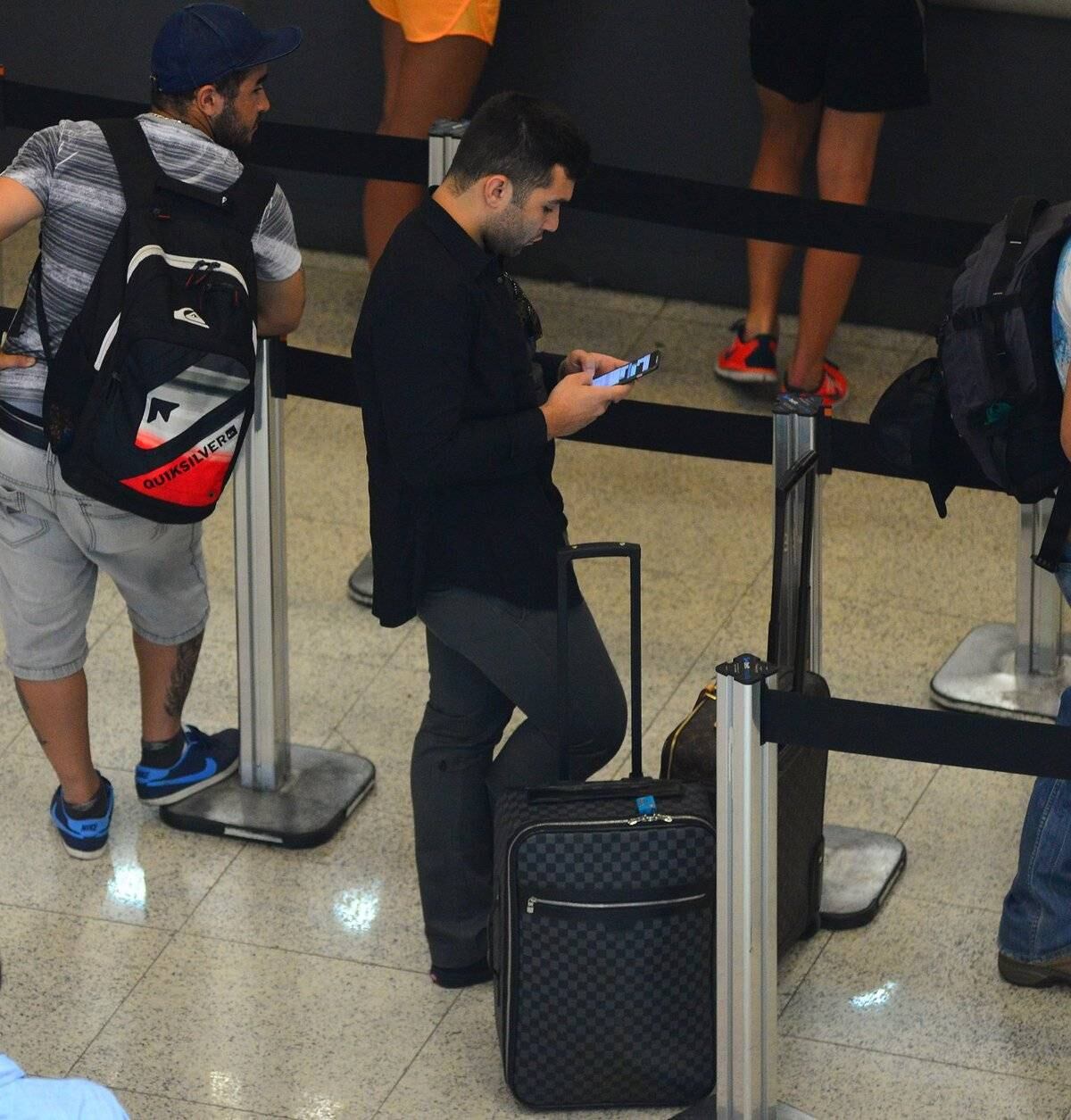 Jonathan optou por um look escuro e verificou o celular enquanto estava na fila do check in
