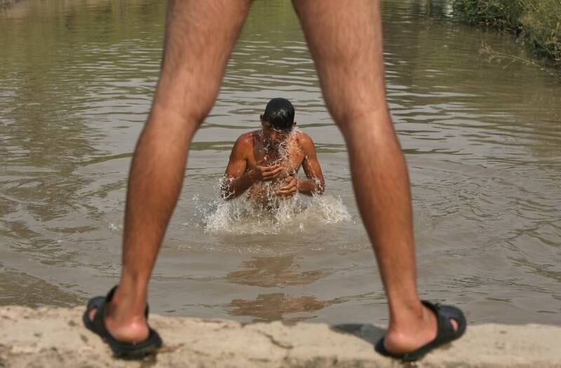 Homem se refresca em um canal durante dia quente em Jammu,
na Índia