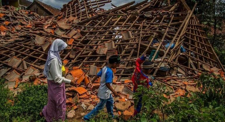 Crianças passam por uma casa que desabou após terremoto, em Java Ocidental