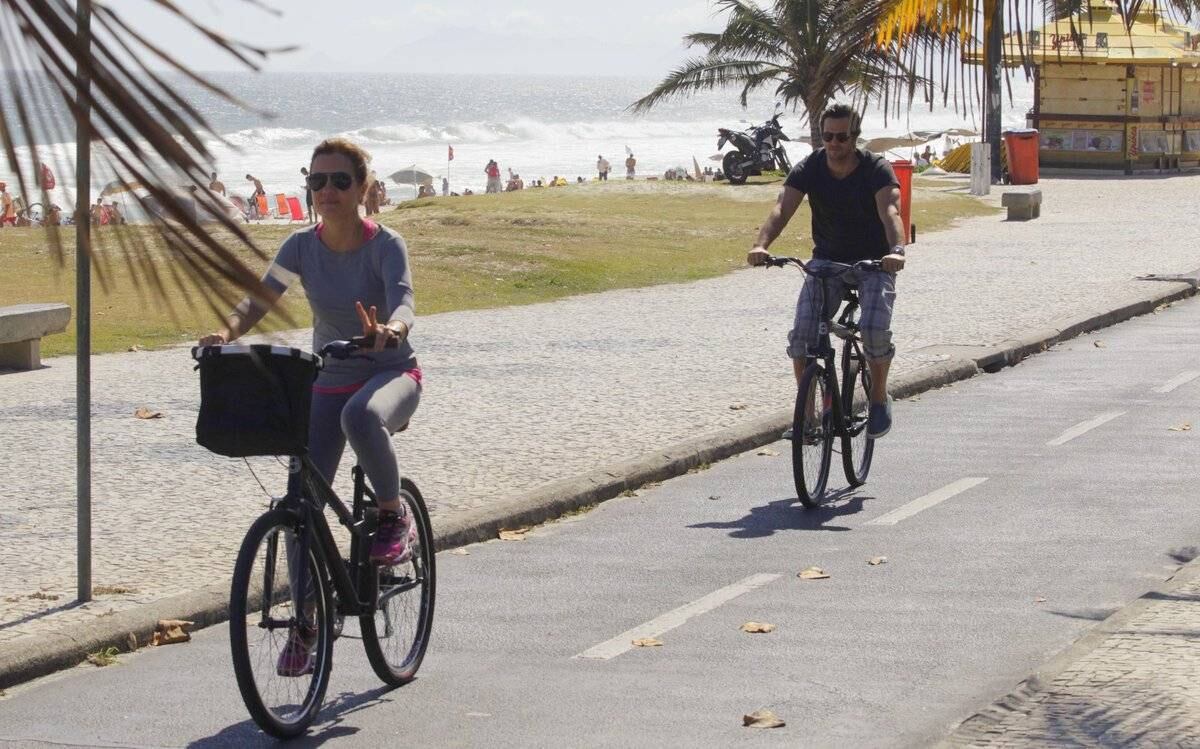 Adriana Esteves e Vladimir Britcha andam de bicicleta na praia da Barra, no Rio