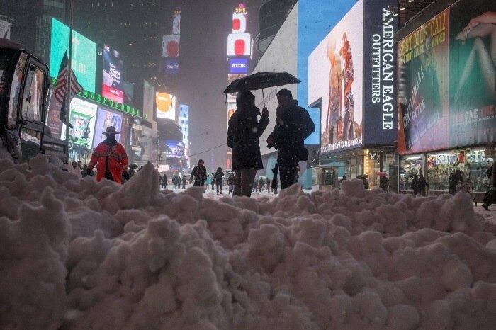 Turistas se protegem da neve sob o guarda-chuva, próximo à neve acumulada na calçada de uma passarela na Times Square, em Nova York