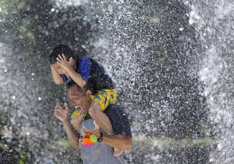 Menino senta nos ombros do
pai para se refrescarem juntos em uma fonte de Tóquio durante dia quente do
verão japonês

 