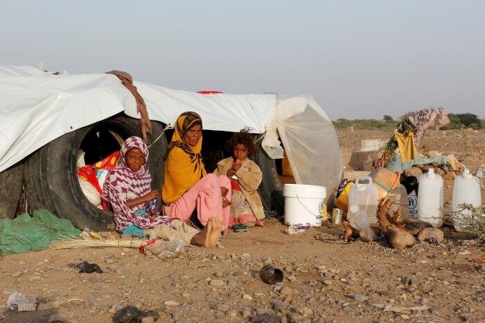 Mulher e suas filhas sentam-se ao lado de sua cabana em um acampamento improvisado para povos internamente deslocados no sul de al-Jarahi, na cidade portuária de Houdieda, Yemen, próxima ao mar Vermelho
