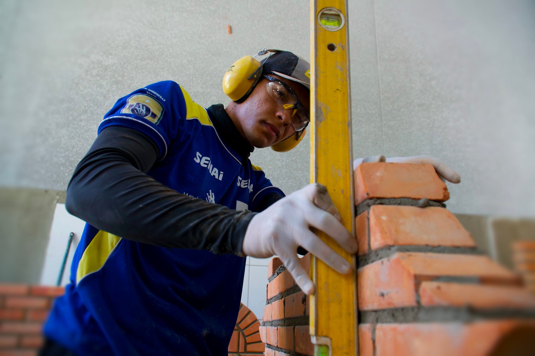 Pedreiro, com proteção nos ouvidos, constrói paredes com ferramentas da construção civil