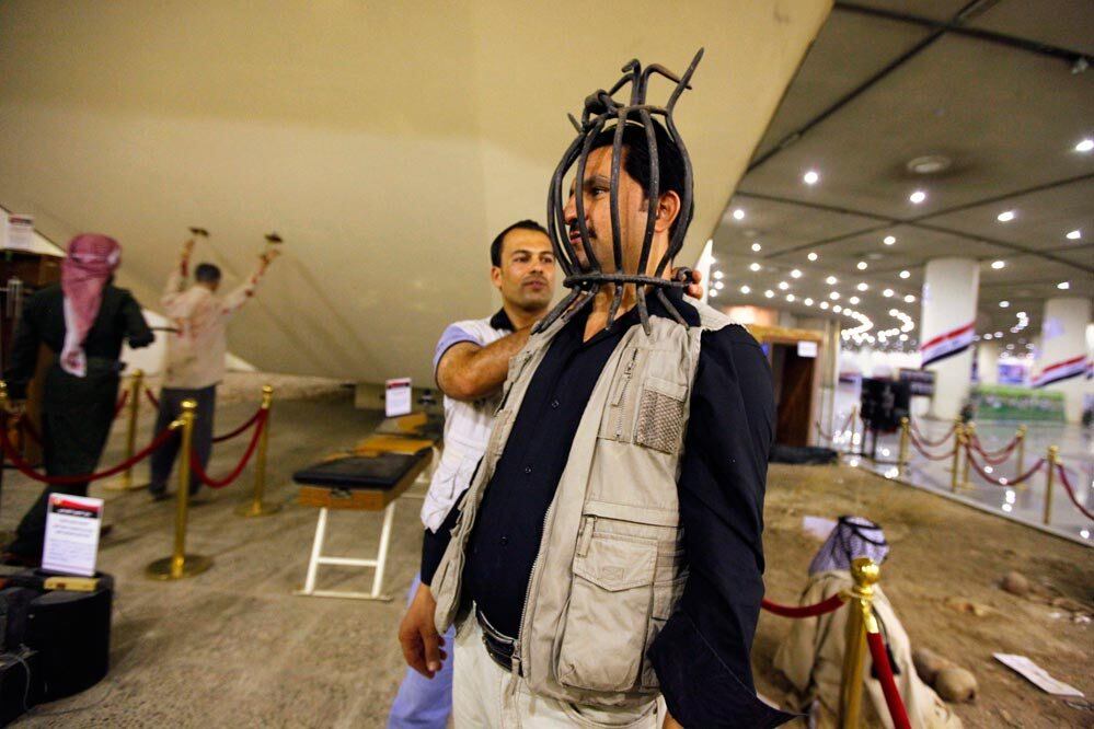 Visitante coloca máscara usada como instrumento de tortura durante o regime de Saddam Hussein