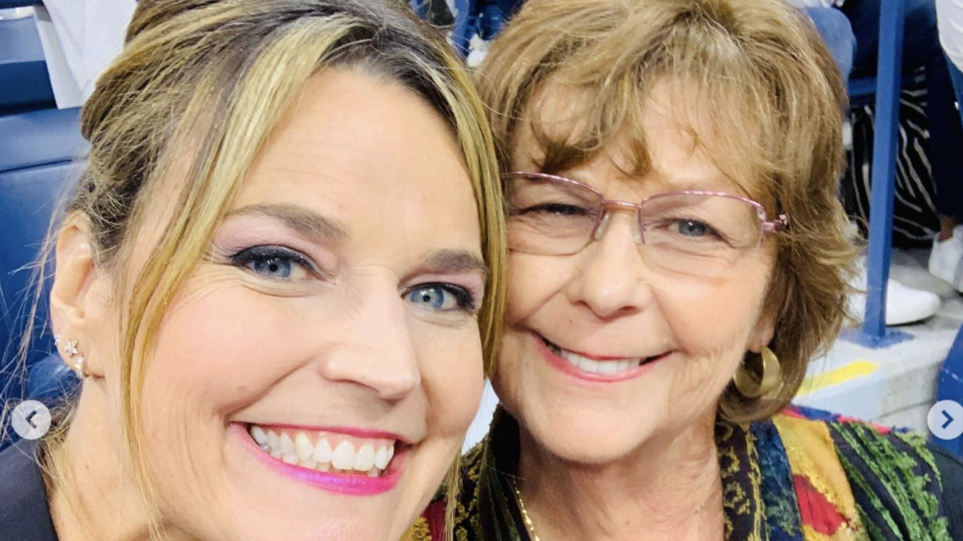 Duas mulheres brancas e loiras, lado a lado. Uma delas, mais jovem, está de cabelo preso, brincos, sorrindo e utiliza batom rosa. Enquanto a outra é mais velha, está de cabelo solto e utiliza óculos de grau.