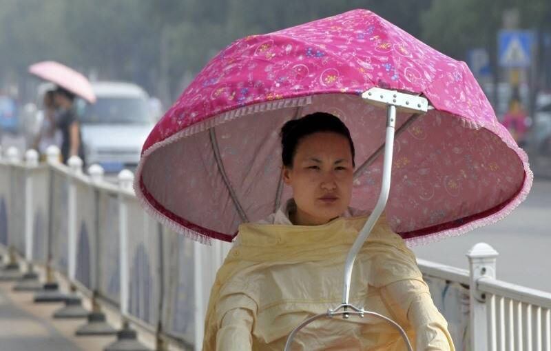 Mulher passeia de bicicleta com guarda-chuva na cabeça em Lianyungang, na China