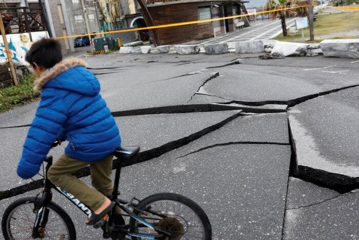 A imagem mostra uma criança andando de bicicleta em uma rua cujo asfalto foi rachado pelo terremoto. Pelo menos 58 pessoas continuam desaparecidas e mais de 260 se feriram