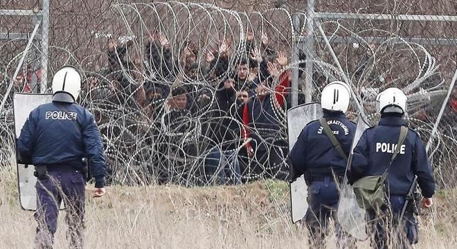 Imigrantes fazem sinal de que se rendem à policiais na fronteira Grécia-Turquia