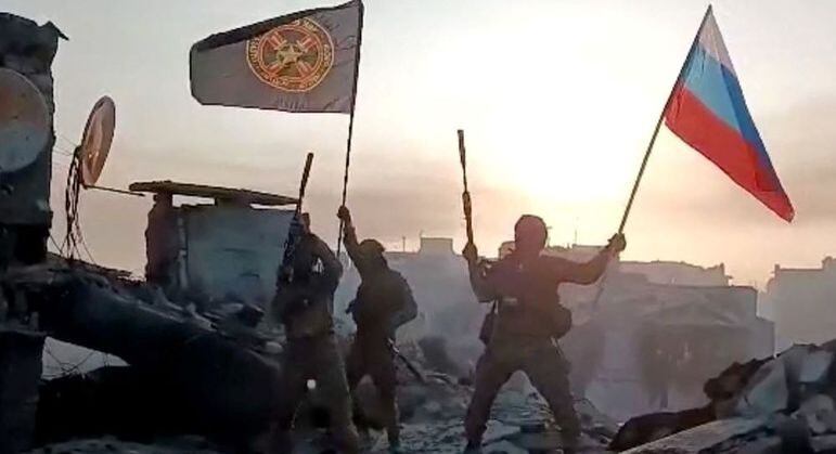 Imagem retirada de um vídeo mostra soldados paramilitares do grupo Wagner com a bandeira russa comemorando a tomada de uma região da cidade de Bakhumut neste sábado (20)